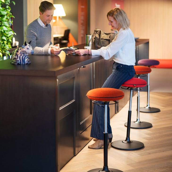 Twee personen genieten van een gesprek op ergonomische VILT Steady krukken aan een hoge bar.