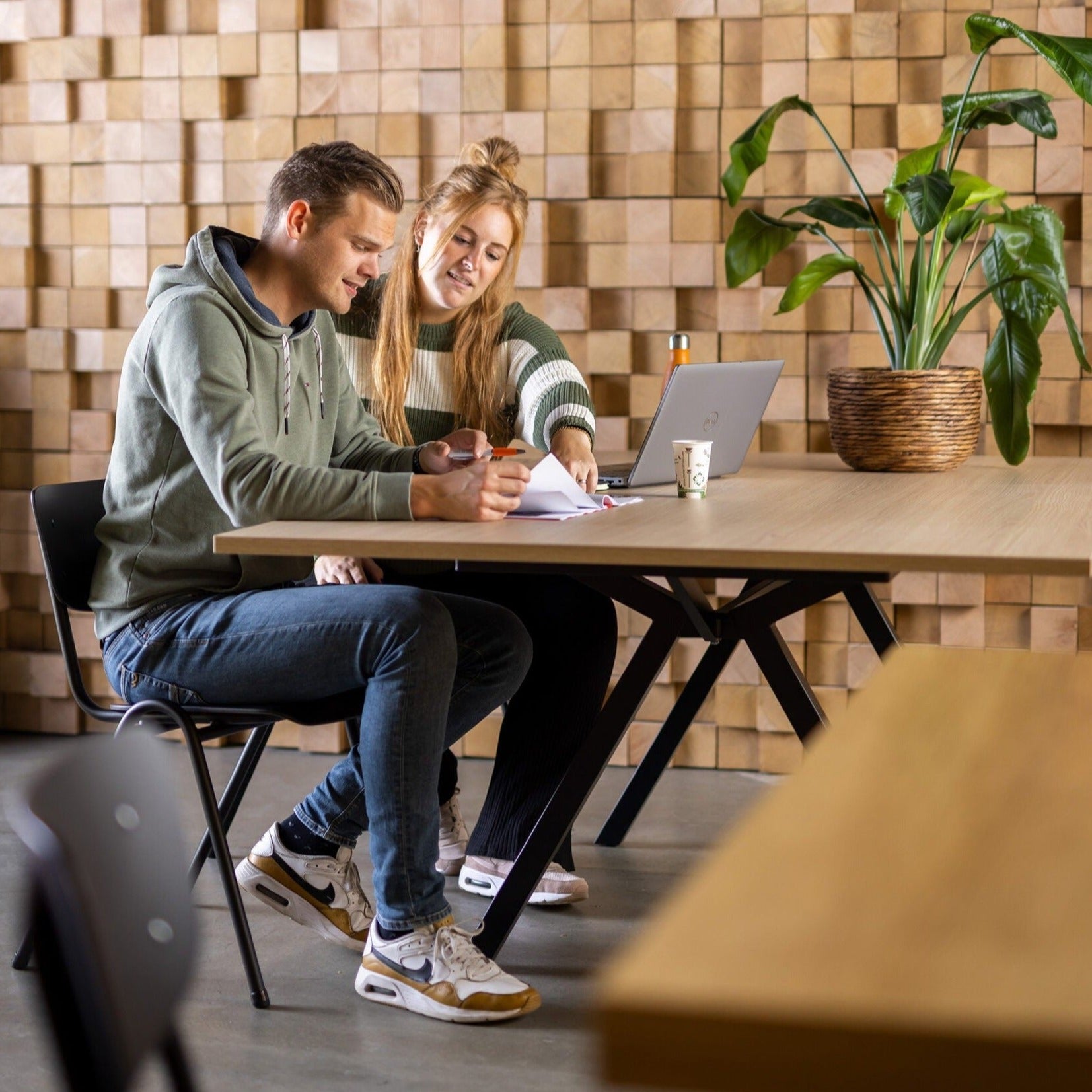 Twee mensen zitten aan een vergadertafel met een laptop, ideaal voor samenwerking en overleg in een moderne werkomgeving.