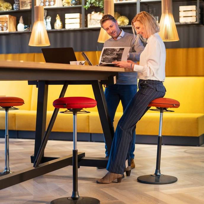 Twee personen op VILT Steady krukken aan een hoge tafel, perfect voor een flexibele werkhouding.