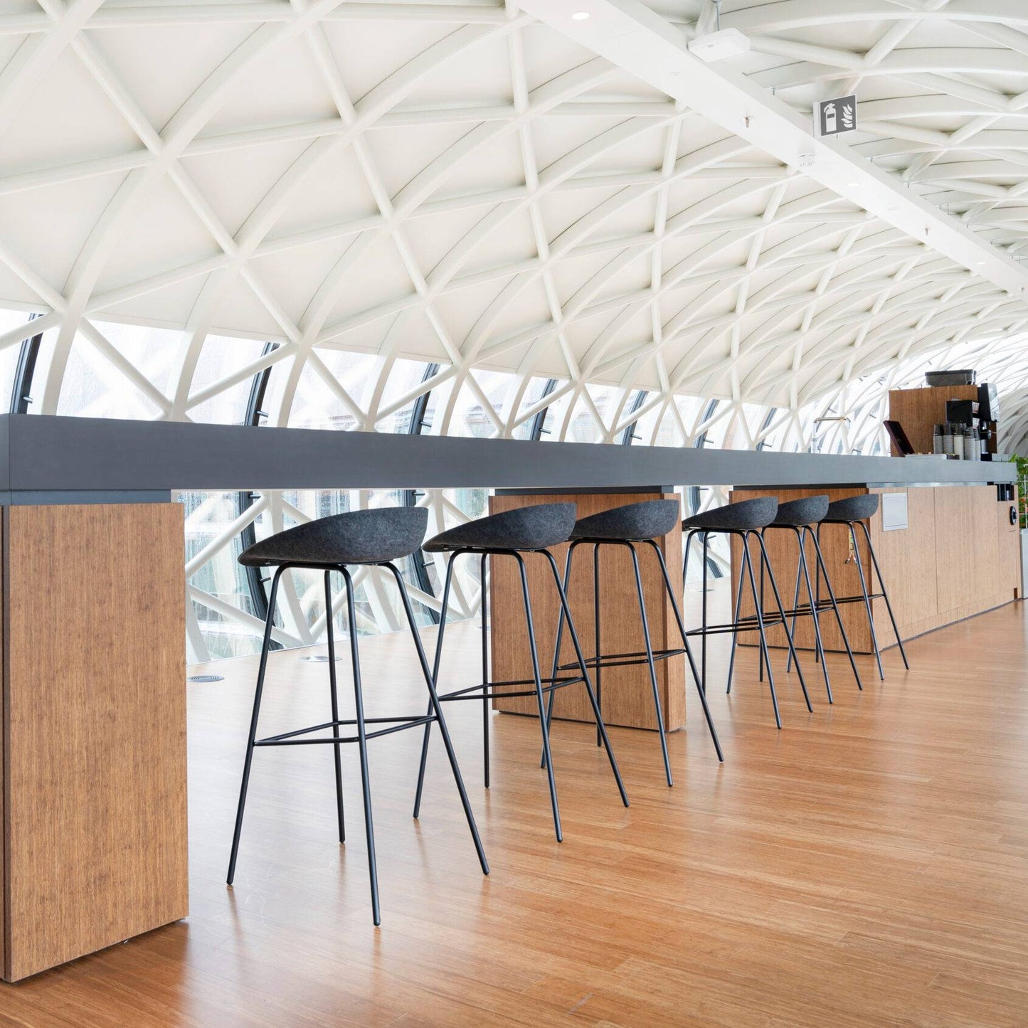 Een moderne tafel met 
zes hoge krukken van gerecycled materiaal en een levendige plant, voor een eco-vriendelijke uitstraling.