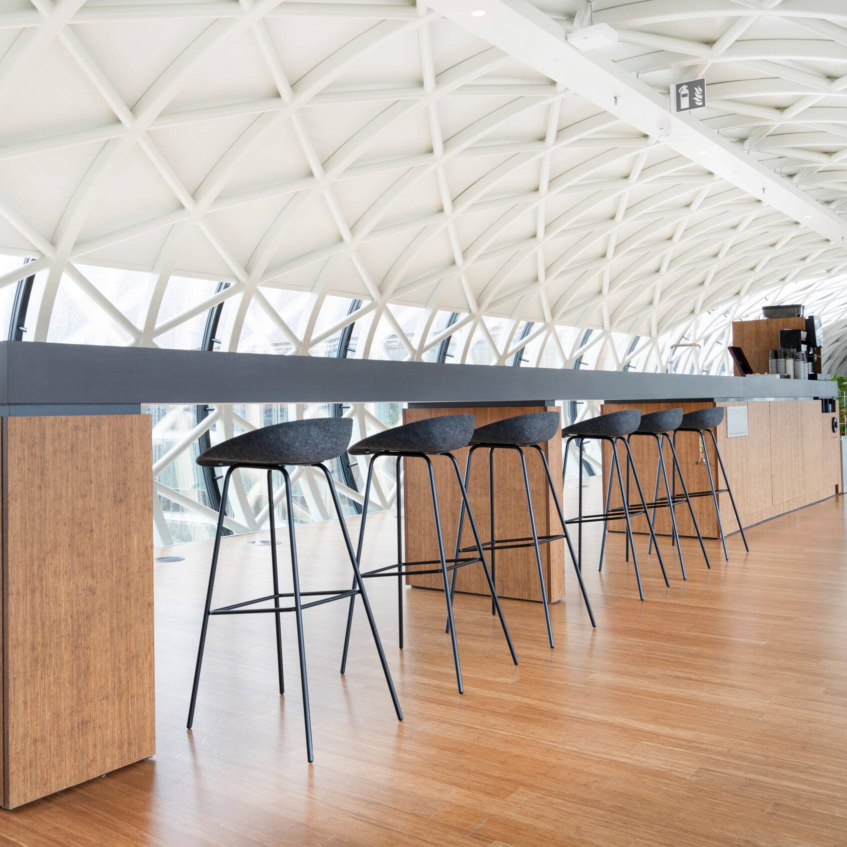 Een moderne tafel met 
zes hoge krukken van gerecycled materiaal en een levendige plant, voor een eco-vriendelijke uitstraling.