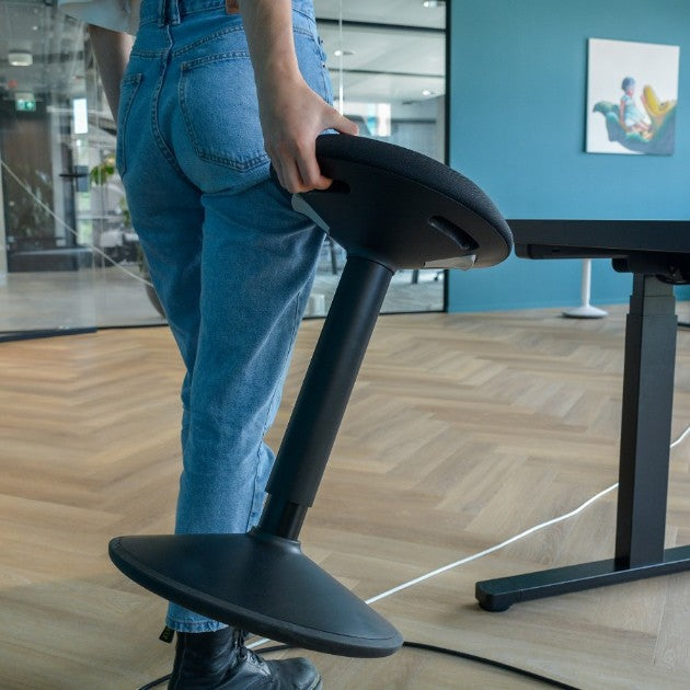 Een persoon op een zwarte wiebelkruk met een laptop, een moderne en ergonomische manier van werken.