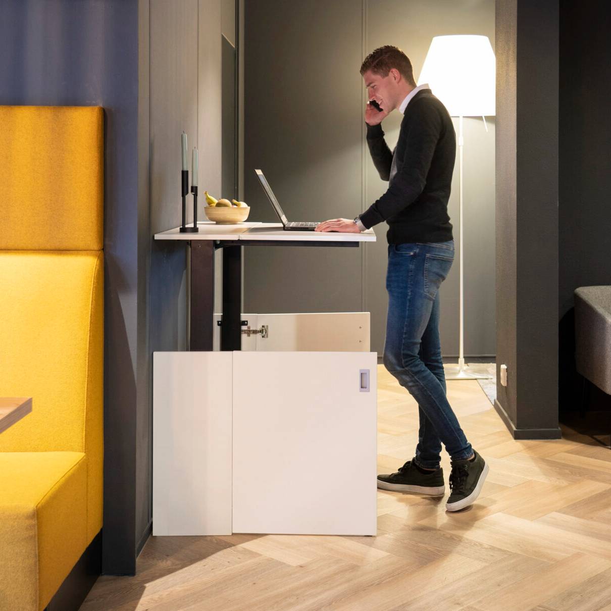 Een man staat aan een bureau met een laptop, genietend van zijn HomeFit thuiswerkplek voor een betere houding.