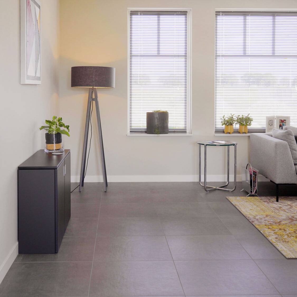 Een moderne woonkamer met een grijze bank, lamp en tafel, geschikt voor een comfortabele thuiswerkervaring.