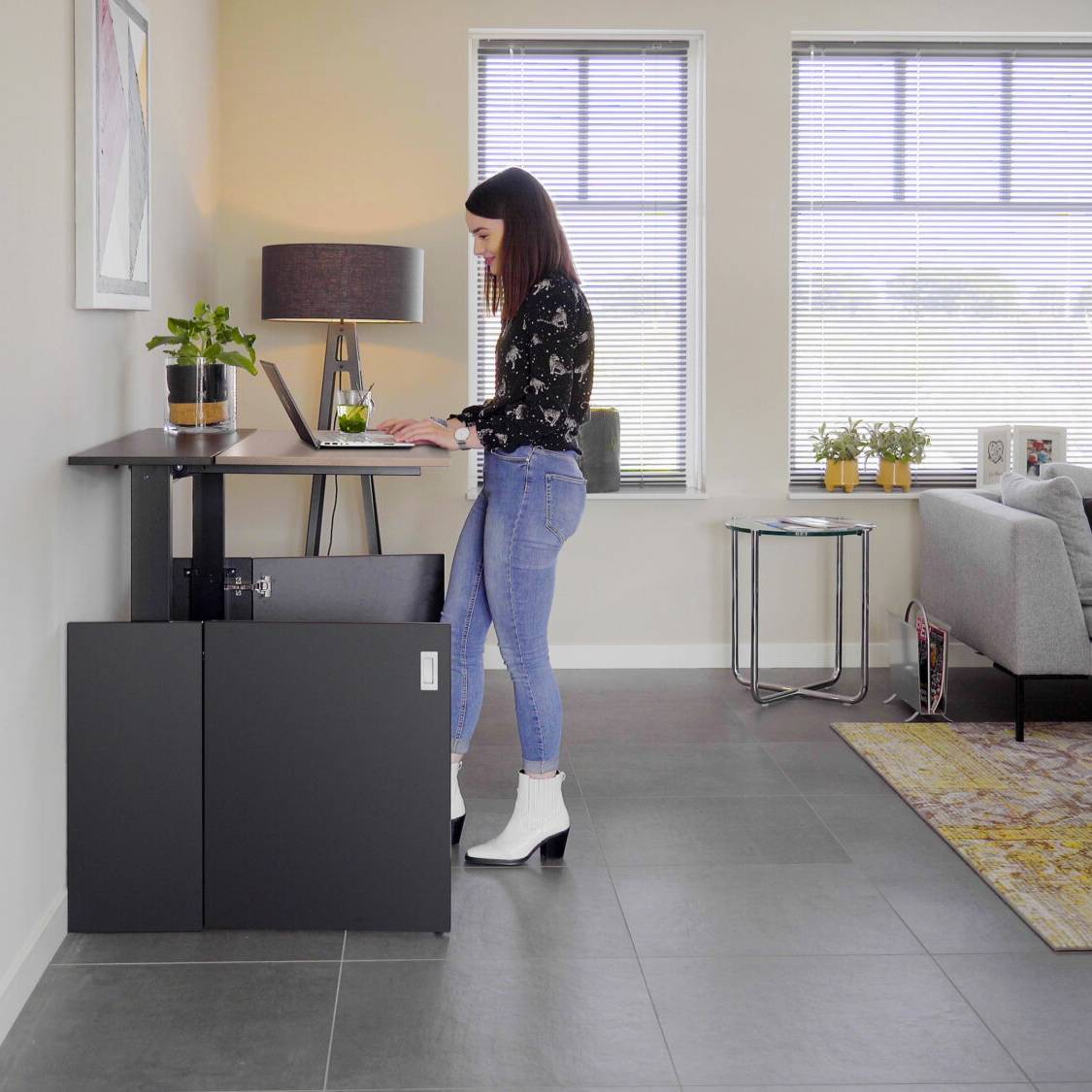 Een vrouw staat bij haar bureau met computer in de gezellige HomeFit thuiswerkplek.